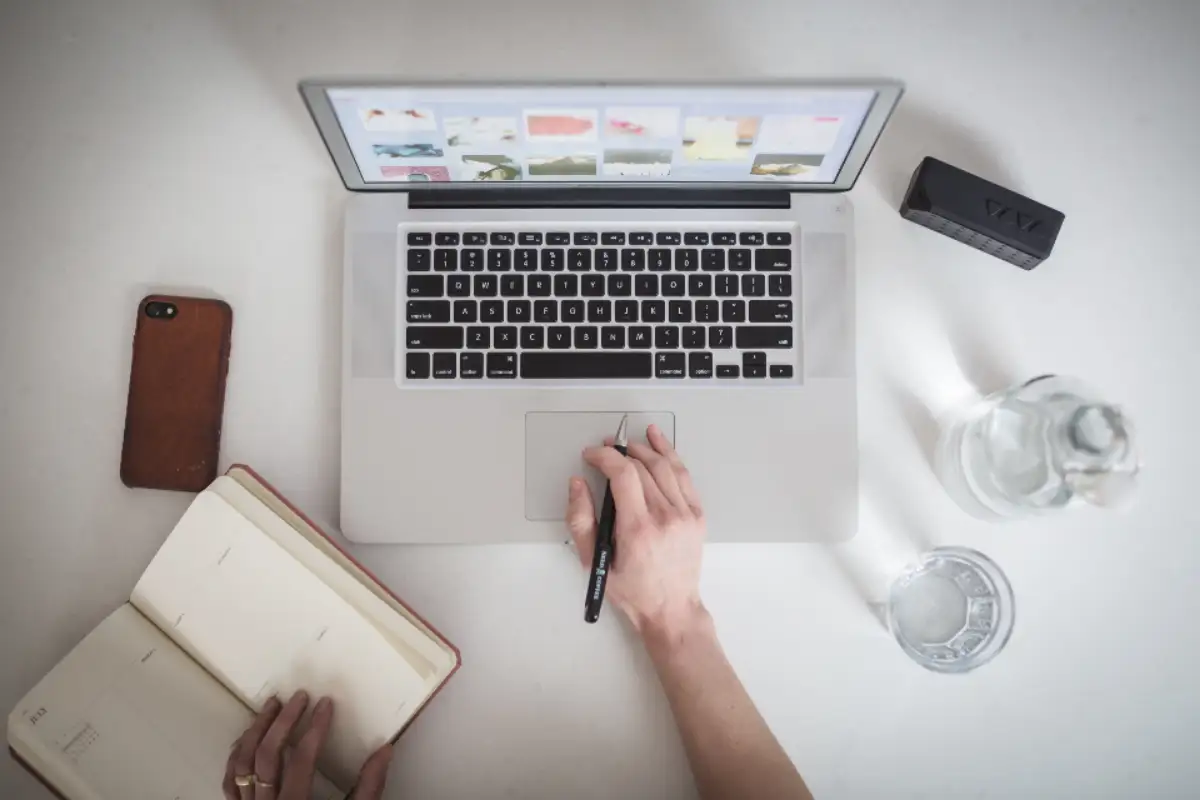 Bureau vu de dessus : ordinateur portable, carnet ouvert et stylo en main