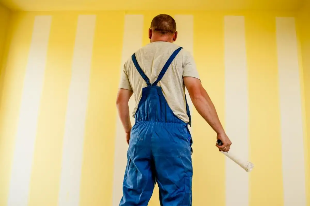 Artisan en salopette devant un mur en cours de peinture
