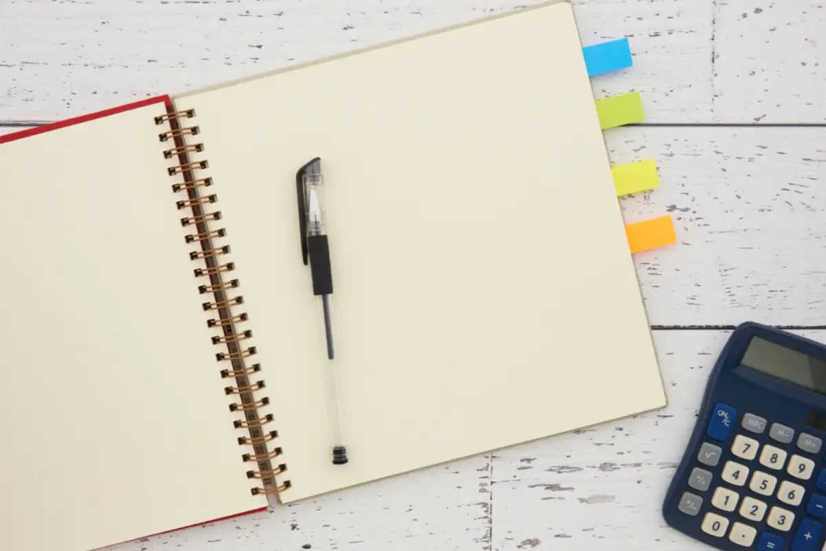 Carnet ouvert, stylo et calculatrice posés sur un plan de travail clair
