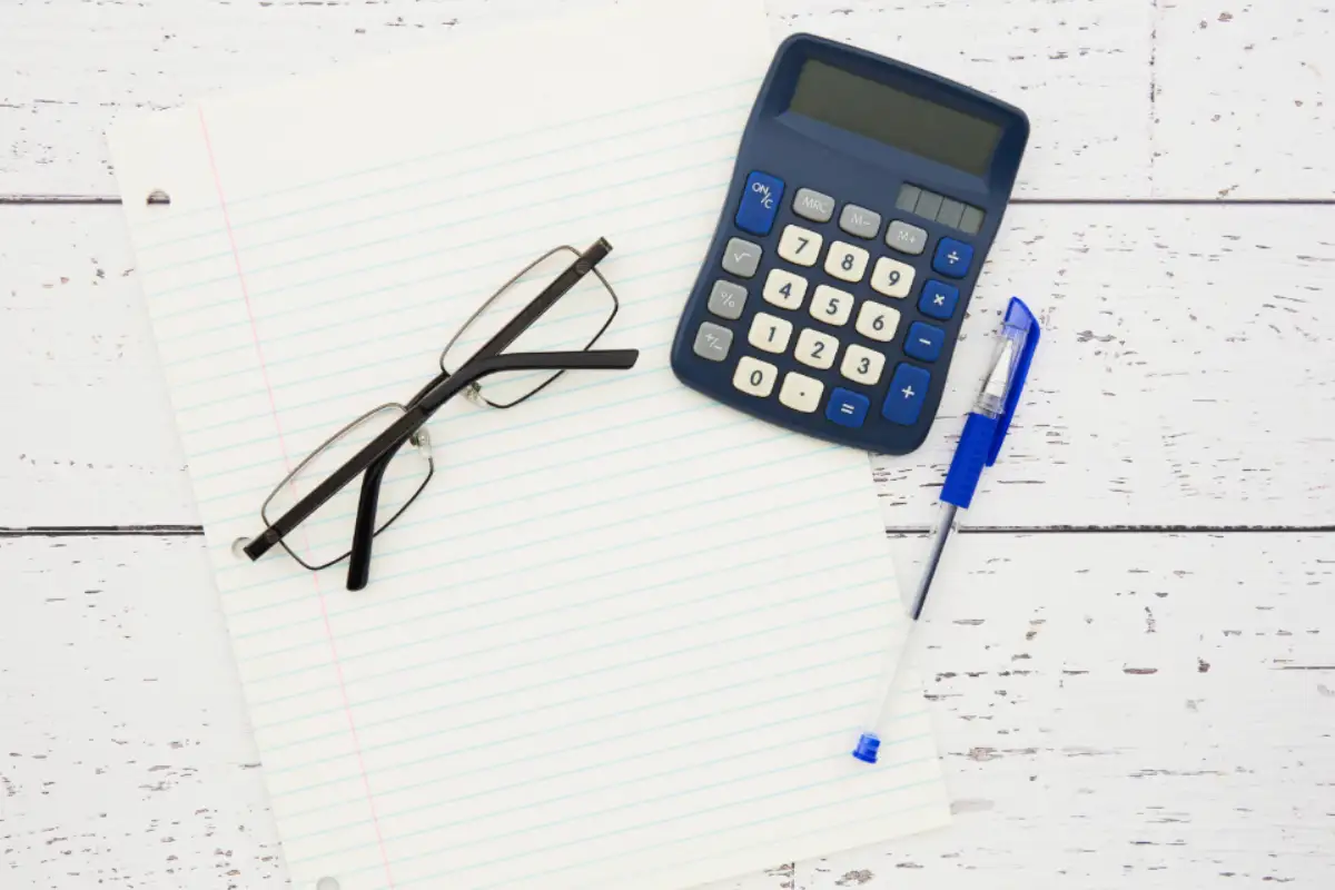 Lunettes, calculatrice et feuille lignée disposées sur un bureau blanc