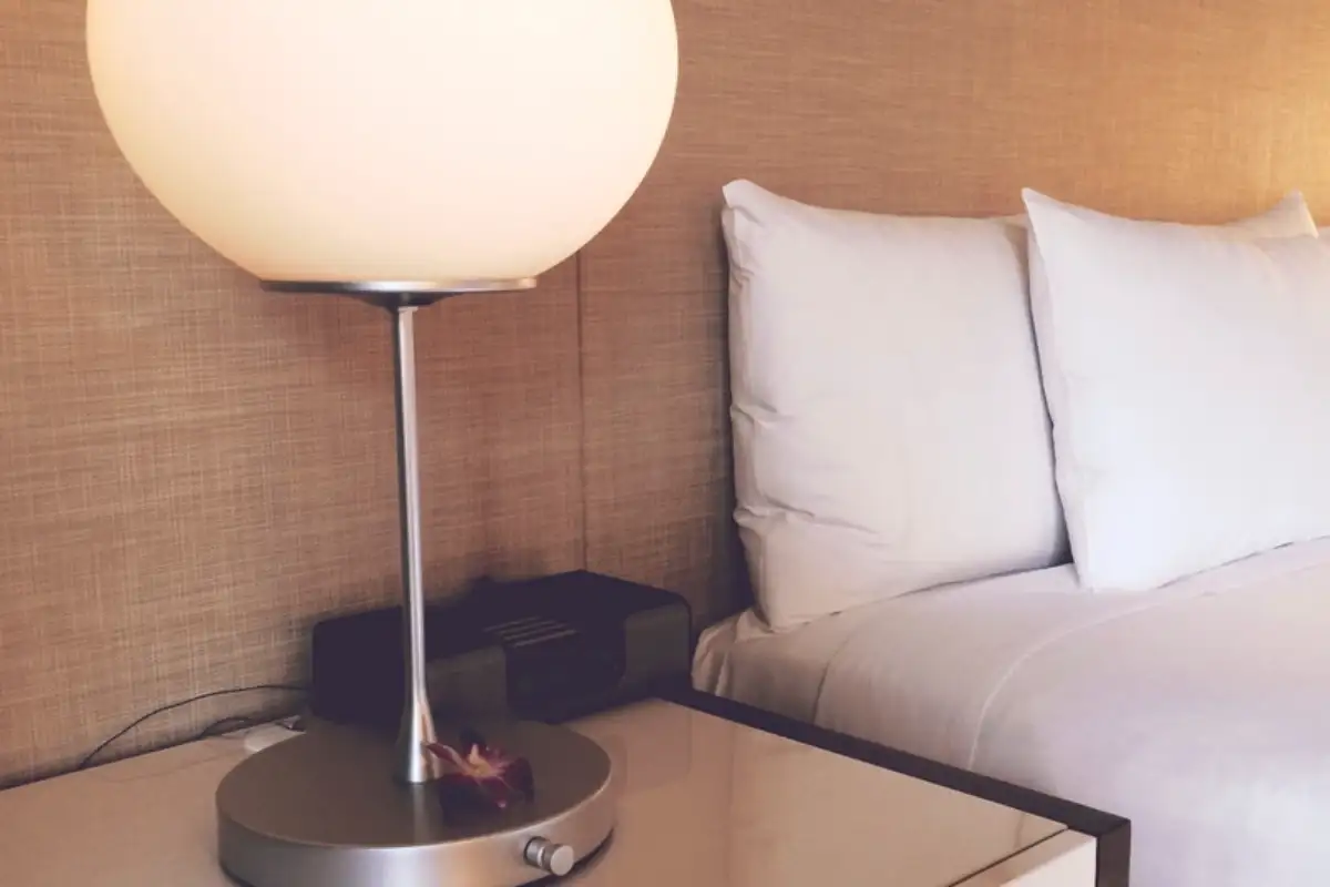 Coin d'une chambre préparée : lampe allumée et oreillers blancs