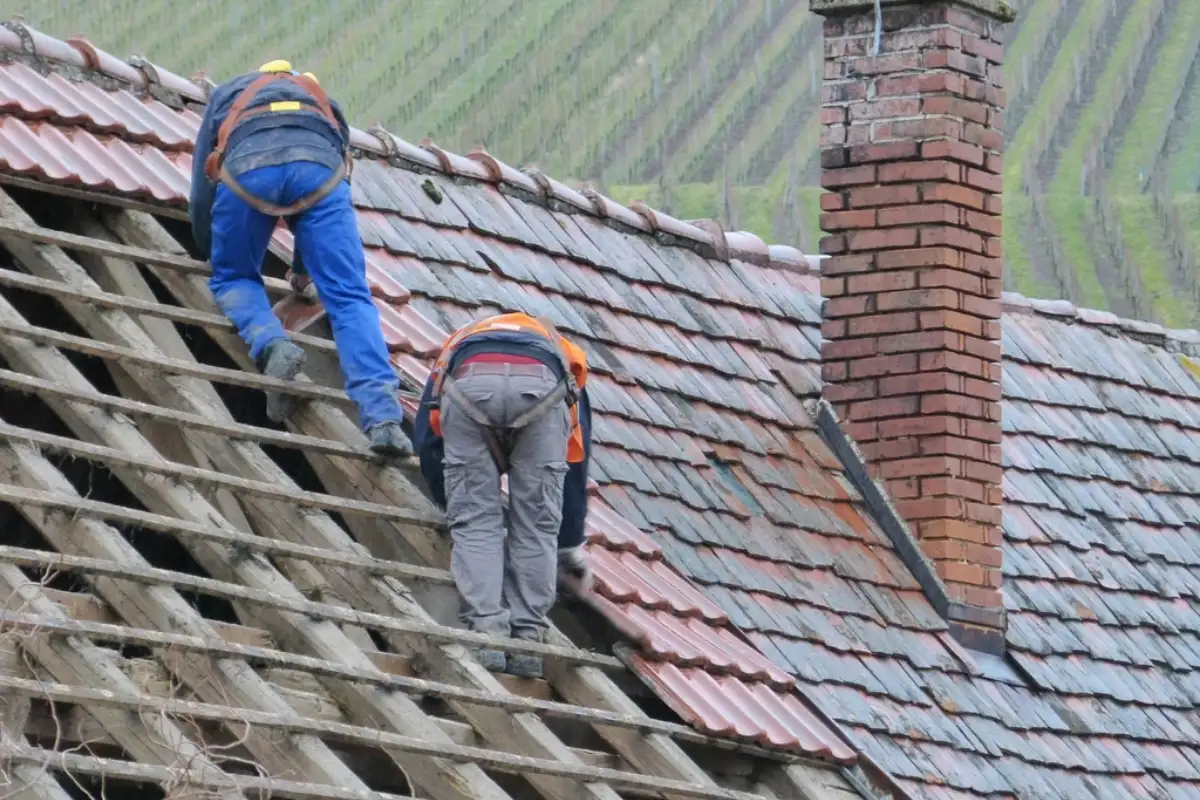 Deux couvreurs en cours de réfection d'une toiture en tuiles, autour d'une souche de cheminée en briques