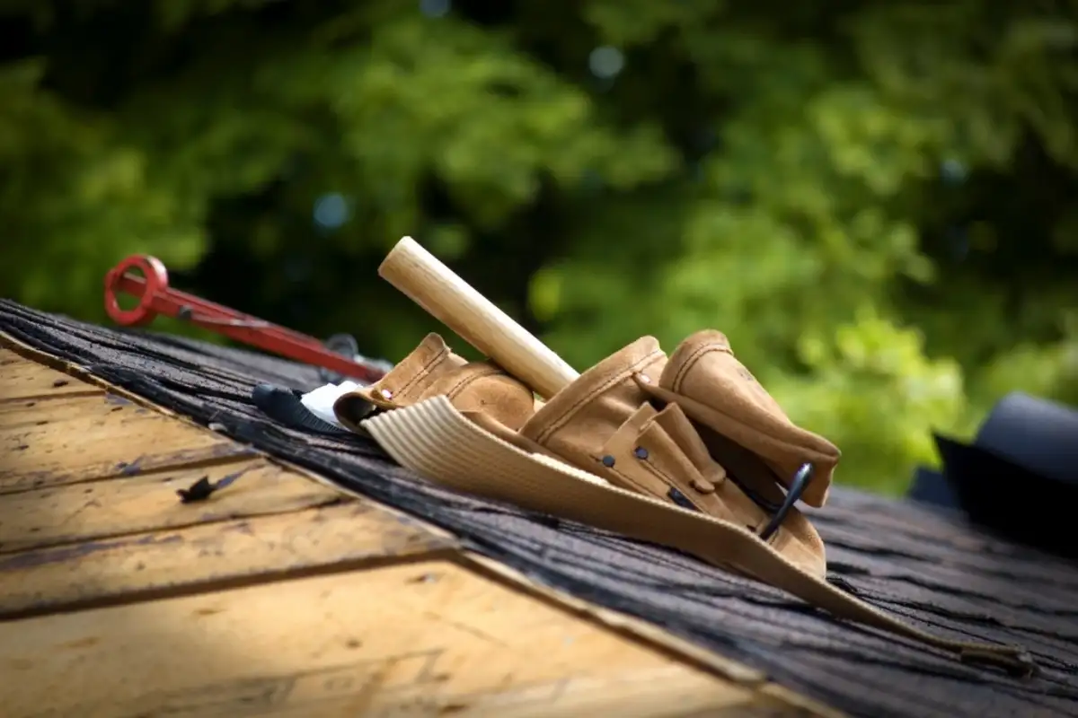 Ceinture à outils et marteau de couvreur posés sur des liteaux, en haut d'un toit