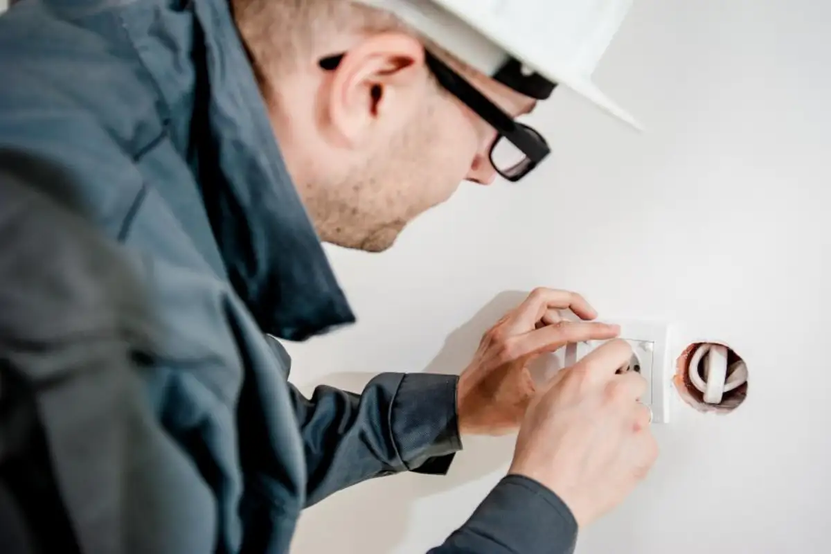Électricien casqué posant un appareillage mural dans un logement
