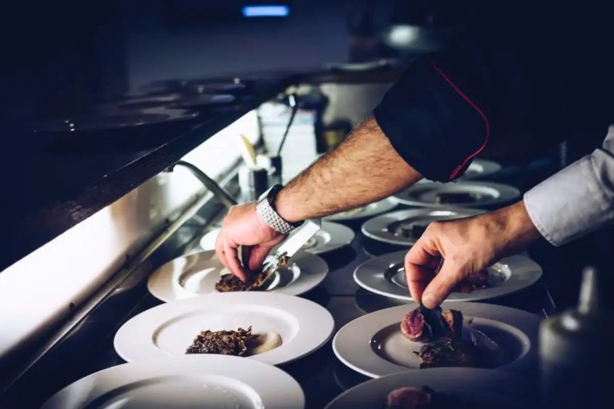 Cuisinier dressant plusieurs assiettes à la pince sur un passe