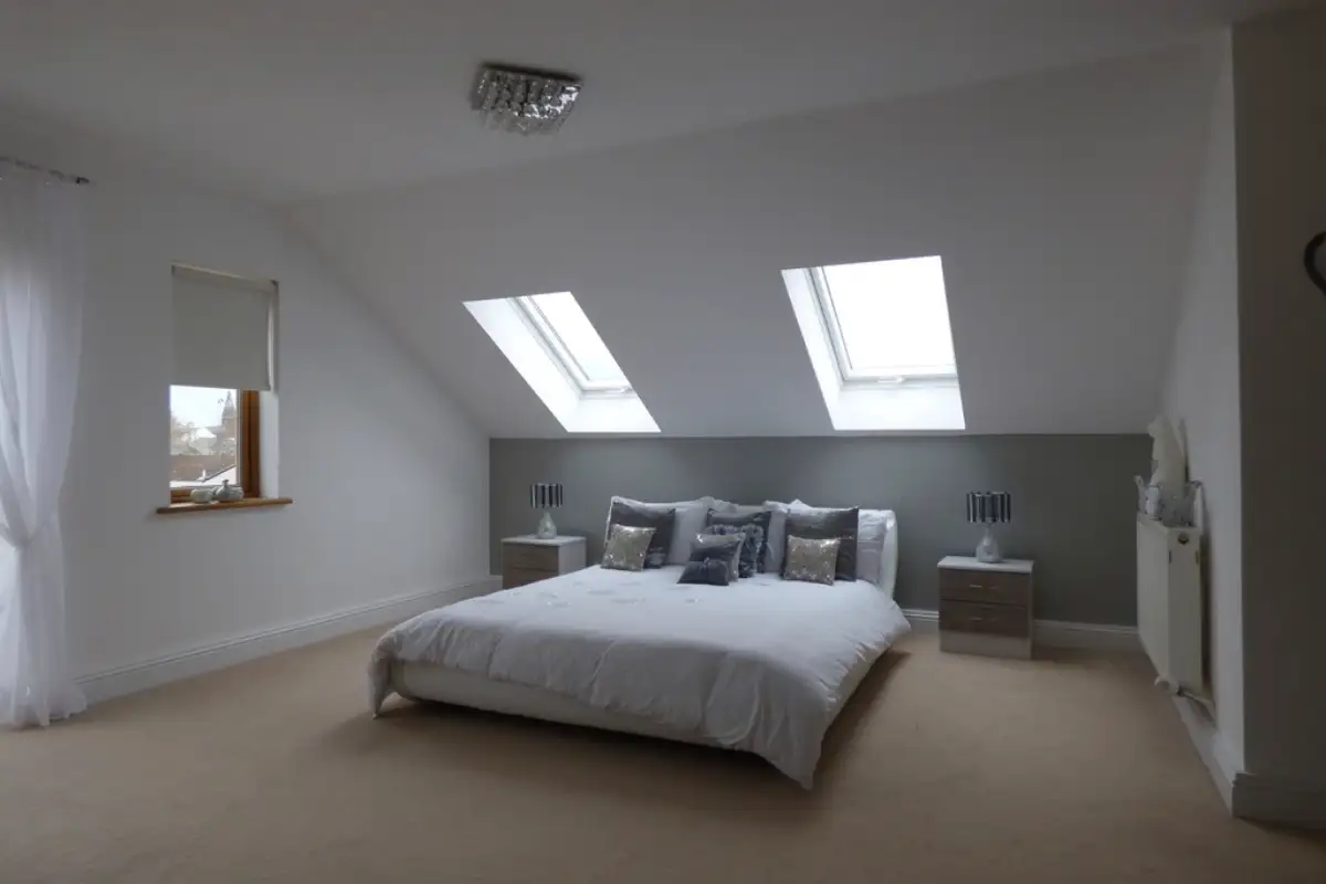 Chambre mansardée sous deux fenêtres de toit, lit fait de blanc