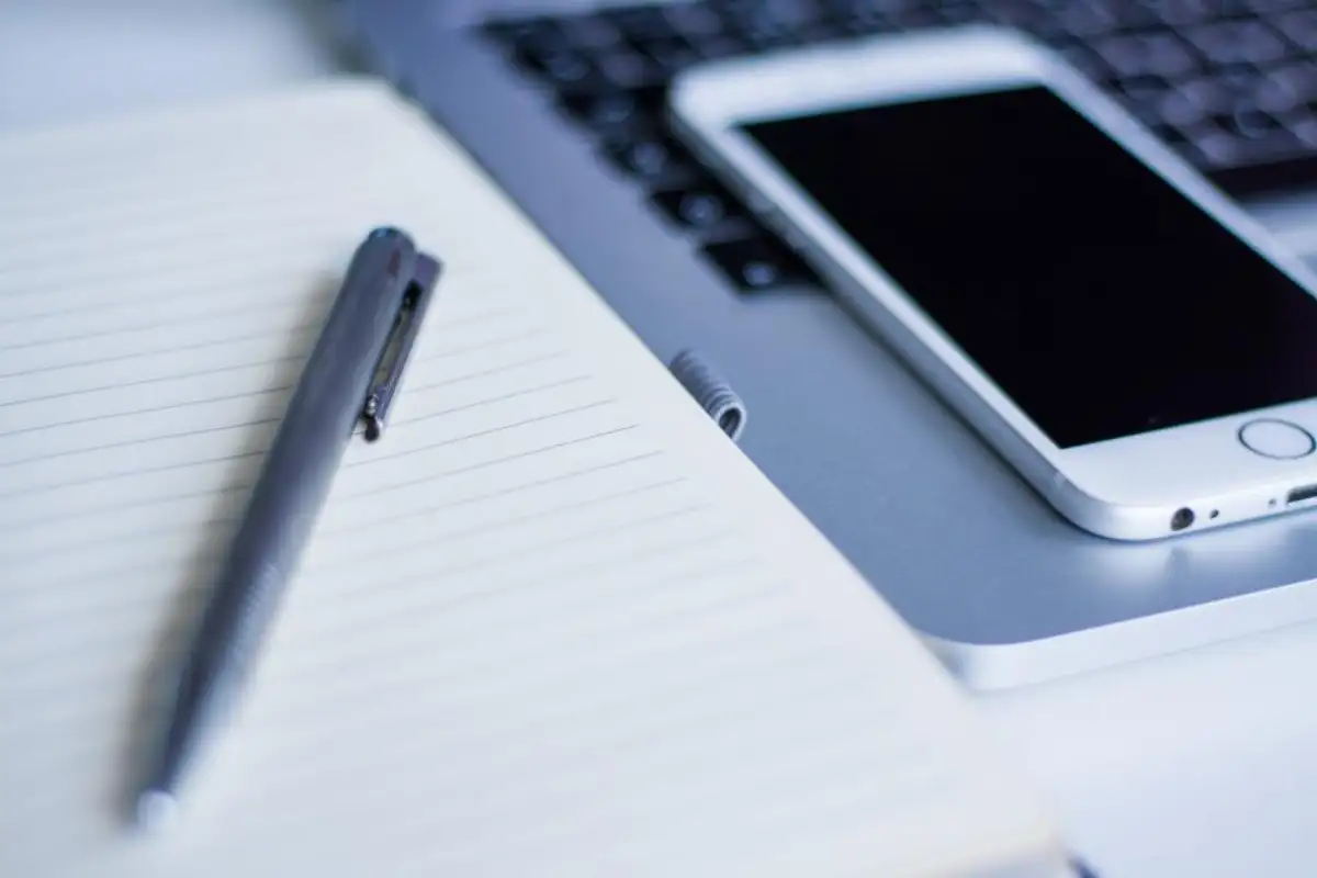 Stylo et téléphone posés sur un carnet ligné, à côté d'un clavier